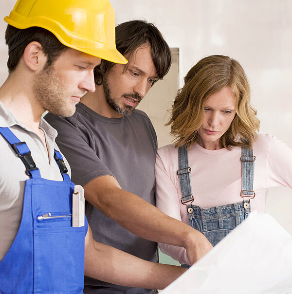 Bauunternehmer mit Helm zeigt Ehepaar einen Bauplan